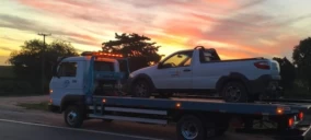 Guincho plataforma transportando uma picape branca em Mucuri, ao entardecer, em uma rodovia.