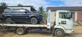 Guincho plataforma transportando um veículo SUV preto em São Mateus, com fundo de área rural e céu parcialmente nublado.