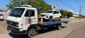 Guincho plataforma transportando um veículo SUV branco em Palmas, estacionado em uma rua.