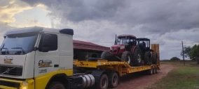 Guincho plataforma transportando dois tratores vermelhos em Belém, em área rural com céu nublado.
