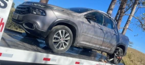 Guincho plataforma transportando um veículo cinza, modelo SUV, em Arcos, com uma roda erguida.