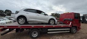 Guincho plataforma vermelho com veículo prata em cima, estacionado em área aberta em Videira, SC.
