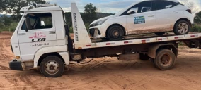 Guincho plataforma transportando um carro branco em Primavera do Leste, em terreno de terra.