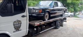 Guincho plataforma em Franco da Rocha transportando um carro preto, estacionado em área de terra.