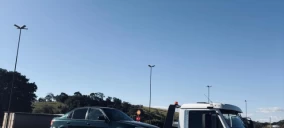Guincho tipo plataforma transportando um veículo sedan verde em Belo Horizonte, em área aberta com céu claro.