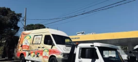 Guincho de plataforma transportando uma van colorida em Belo Horizonte, com céu claro ao fundo.