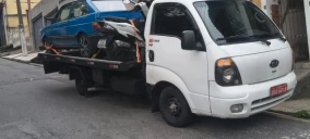 Guincho plataforma branco transportando um carro azul em Osasco, estacionado em uma rua.