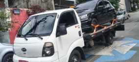 Guincho plataforma em Osasco transportando um veículo preto, estacionado em uma rua com sinalização.