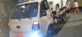 Guincho plataforma branco transportando uma caminhonete branca em Osasco, estacionado em via pública à noite.