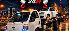 Guincho plataforma branco transportando um carro branco em Osasco, com fundo de cidade iluminada à noite.