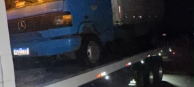 Guincho plataforma transportando um caminhão Mercedes azul em Recife, à noite.
