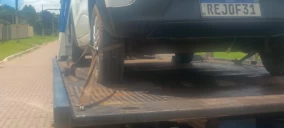 Guincho plataforma transportando um veículo de cor escura em Novo Gama, com uma roda erguida.