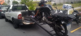Guincho tipo plataforma transportando uma motocicleta preta em Santo André, com veículo estacionado na rua.