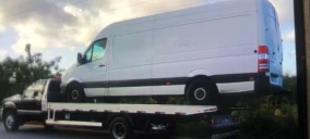 Guincho plataforma transportando uma van branca em Porto Calvo, com o veículo erguido na parte traseira.