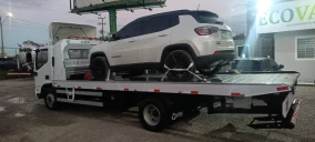 Guincho plataforma transportando um veículo SUV branco em Ibiúna, estacionado em um local com iluminação artificial.