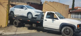 Guincho plataforma transportando um carro branco em Ubatuba, com parte do veículo na calçada e parte na rua.
