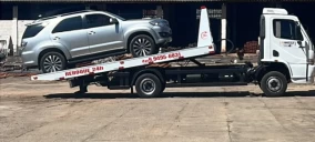 Guincho plataforma com veículo prata carregado, estacionado em área de serviço em Crato.