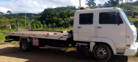 Guincho plataforma branco estacionado em área rural de Jaguaruna, sem veículo transportado visível.