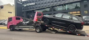 Guincho plataforma em Caxias do Sul transportando um veículo preto, estacionado em frente a uma concessionária.