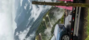 Guincho plataforma em Caxias do Sul transportando um carro cinza em uma área montanhosa com neblina.