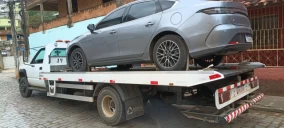 Guincho plataforma transportando um carro sedã cinza em Carmo, estacionado em uma rua pavimentada.