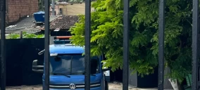 Guincho azul estacionado atrás de uma grade, em área com vegetação, em Olinda.