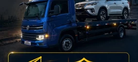 Guincho plataforma azul transportando um veículo branco em Olinda, estacionado em via urbana.