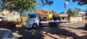 Guincho plataforma branco estacionado em rua de Piraju, transportando um caminhão amarelo.