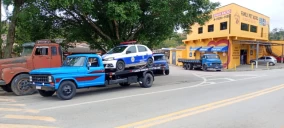Guincho plataforma azul transportando um carro branco em São Roque, próximo a um estabelecimento comercial.