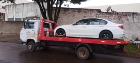 Guincho plataforma transportando um carro branco em Cascavel, estacionado em uma rua.