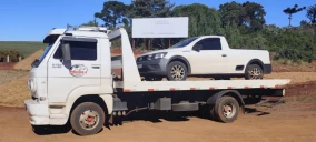 Guincho plataforma branco transportando uma picape branca em Ibema, com fundo de terra e vegetação.