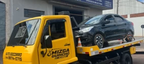 Guincho plataforma amarelo transportando um carro preto em Campo Mourão, estacionado em frente a um estabelecimento.
