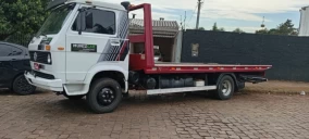 Guincho plataforma estacionado em Carazinho, com cabine branca e carroceria vermelha, sem veículo transportado visível.