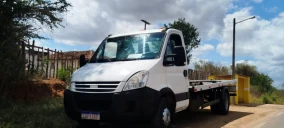 Guincho plataforma estacionado em Utinga, com veículo branco visível na carroceria.