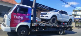 Guincho plataforma transportando uma caminhonete branca em São Ludgero, estacionado em via pública.