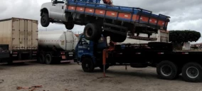 Guincho de plataforma levantando uma caminhonete branca em Capim Grosso, com outros caminhões ao fundo.
