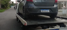 Guincho plataforma transportando um carro cinza, estacionado em uma rua de Praia Grande.