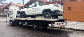 Guincho plataforma transportando uma caminhonete branca em Praia Grande, estacionado em uma rua residencial.