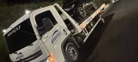 Guincho plataforma em Juiz de Fora transportando um carro preto, à noite, em uma via.