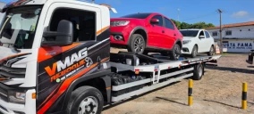 Guincho plataforma em Teresina transportando um veículo vermelho, estacionado em área com outros carros ao fundo.